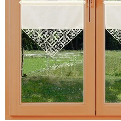 Ein holzgerahmtes Fenster ist oben teilweise mit einem weißen Stoffvorhang versehen. Der Vorhang weist ein dreieckiges Spitzenmuster mit Blumenmotiven auf. Durch das Fenster sind grünes Gras und ein Zaun zu sehen, was auf einen Garten oder einen Außenbereich hindeutet.