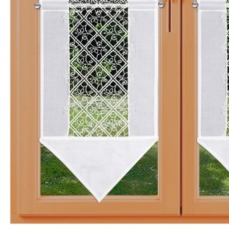 Ein Fenster mit Holzrahmen und zwei Glasscheiben, die jeweils von einem weißen durchsichtigen Vorhang mit Rautenmuster und floraler Stickerei im oberen Bereich bedeckt sind. Die Vorhänge haben durchgehende weiße dreieckige Abschnitte, die unten nach unten zeigen. Außerhalb des Fensters ist Gras zu s