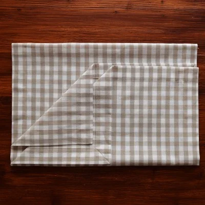 Eine gefaltete beige-weiß karierte Stoffserviette liegt auf einer dunklen Holzfläche, wobei eine Ecke ordentlich umgeschlagen ist, um die Unterseite zu zeigen.