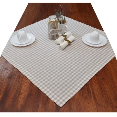 Ein Holztisch mit einem beige-weiß karierten Tischtuch, gedeckt mit zwei Tassen und Untertassen, drei gerollten Servietten, einem Glas und weißen Behältern mit verschiedenem Besteck.