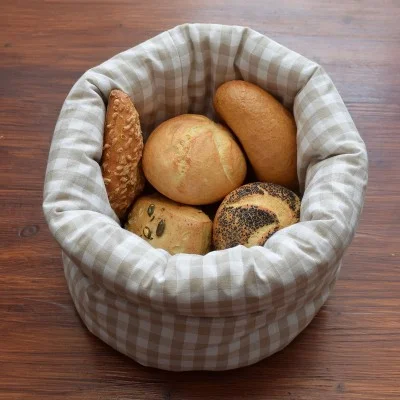 In einem mit Stoff ausgekleideten Korb mit Karomuster liegen verschiedene Brötchen, darunter besaitete und unbesaitete Sorten, auf einer Holzunterlage.