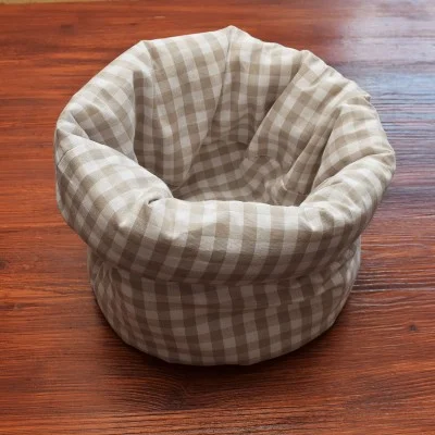 Ein beige und weiß karierter Stoffkorb steht auf einem Holztisch. Der Korb ist weich, rund und hat einen umklappbaren Rand.