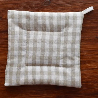 Ein beige-weiß kariert gemusterter, quadratischer Topflappen aus Stoff mit einer Schlaufe in der Ecke, der auf eine hölzerne Unterlage gestellt wird.