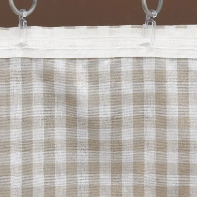 Nahaufnahme eines Vorhangs aus durchsichtigem Stoff mit beige-weißem Gingham-Karomuster. Der Vorhang ist an zwei Metallringen mit durchsichtigen Kunststoffhaken aufgehängt, die an einem weißen Stoffkopf befestigt sind. Der Hintergrund ist einfarbig braun.