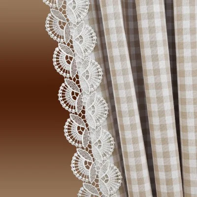 Nahaufnahme eines beige-weiß karierten Vorhangs mit einer dekorativen weißen Spitzenbordüre entlang der Kante vor einem braunen Hintergrund mit Farbverlauf.