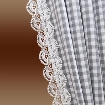 Nahaufnahme von grau-weißem Gingham-Stoff mit einer dekorativen weißen Spitzenborte entlang des Randes vor einem Hintergrund mit braunem Farbverlauf.