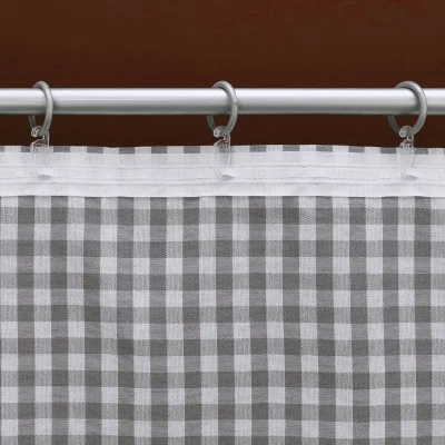 Eine Nahaufnahme eines grau-weiß karierten Vorhangs, der an einer Metallstange mit runden silbernen Ringen hängt. Die Oberseite des Vorhangs hat eine weiße Kopfleiste. Der Hintergrund ist einfarbig braun. Das Bild konzentriert sich auf das Muster und die Details der Aufhängung des Vorhangs.