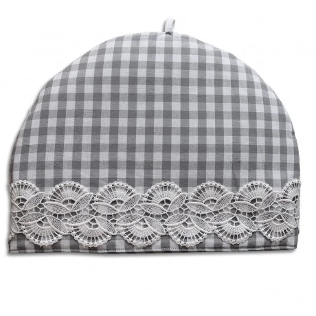 Ein kuppelförmiger Teewärmer mit grau-weißem Gingham-Muster, verziert mit einem breiten Band aus filigraner weißer Spitze am unteren Rand. Oben in der Mitte ist eine kleine Schlaufe angebracht, um die Handhabung zu erleichtern. Der Hintergrund ist einfarbig weiß.