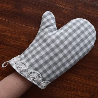 Eine Hand, die einen grau-weiß karierten Topfhandschuh mit weißer Spitzenverzierung an der Manschette trägt, ruht auf einer hölzernen Oberfläche.