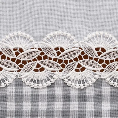 Ein Streifen filigraner weißer Spitze mit floralen und fächerartigen Mustern liegt waagerecht auf einem Hintergrund, der oben in durchsichtigen grauen Stoff und unten in einen grau-weiß karierten Stoff unterteilt ist. Die Spitze sorgt für Kontrast und dekorative Details.