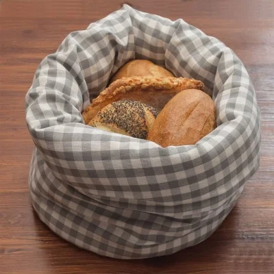In einem grau-weiß karierten Stoffkorb liegen verschiedene Brotsorten, darunter ein Mohnbrötchen, ein runder Laib und ein Gebäckstück, auf einer Holzunterlage.