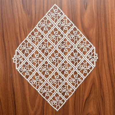 Ein weißes, rautenförmiges Spitzendeckchen mit einem geometrischen Muster aus ineinandergreifenden Quadraten und floralen Motiven ruht auf einer braunen Holzoberfläche. Die Spitze weist detaillierte, symmetrische Muster auf, die handwerklich gut verarbeitet sind.