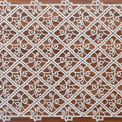 Weißer Spitzentischläufer mit einem Rautengittermuster mit integrierten Blumenmotiven auf einer Holzoberfläche. Jeder Rautenbereich enthält komplizierte, wirbelnde Muster, die zum detaillierten Aussehen des Tischläufers beitragen.