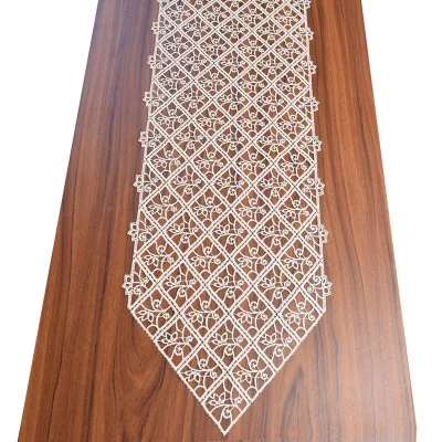 Ein dunkler Holztisch mit einem weißen Spitzentischläufer, der ein detailliertes Rauten- und Blumenmuster aufweist. Der Läufer läuft am Ende spitz zu und ist mittig auf der glatten Holzoberfläche angebracht.