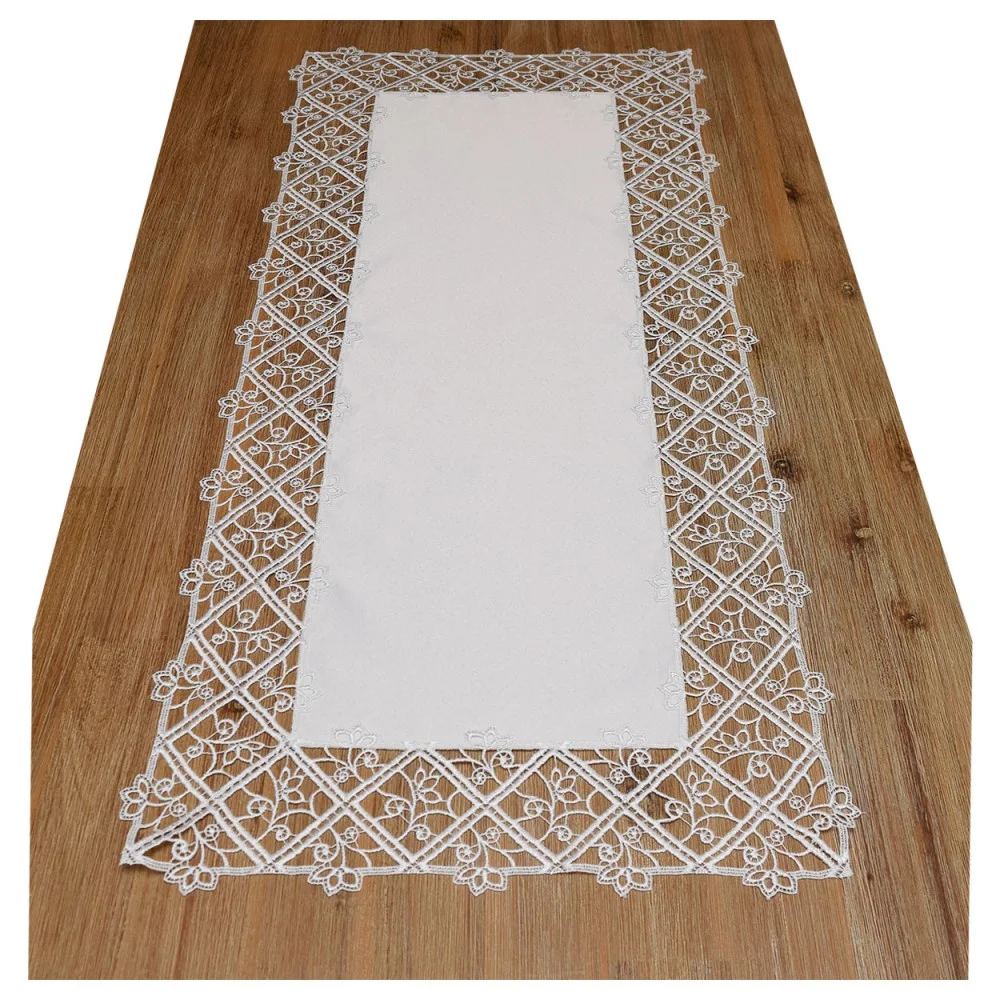 Ein rechteckiger weißer Tischläufer wird auf einem Holztisch präsentiert. Er weist eine komplizierte Spitzenbordüre mit Blumenmustern auf, die ein geometrisches Rautenmuster bilden, das den einfarbigen weißen Stoff in der Mitte umgibt.