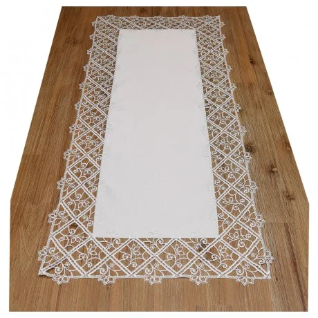 Ein rechteckiger weißer Tischläufer wird auf einem Holztisch präsentiert. Er weist eine komplizierte Spitzenbordüre mit Blumenmustern auf, die ein geometrisches Rautenmuster bilden, das den einfarbigen weißen Stoff in der Mitte umgibt.