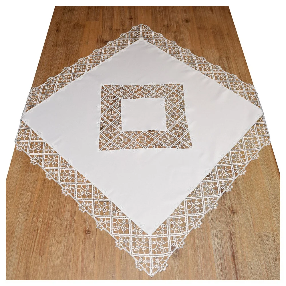 Ein weißes, quadratisches Tischtuch mit detaillierten Spitzenbordüren und ein passendes, mit Spitze eingefasstes Quadrat, das diagonal auf einem Holzboden liegt. Die Spitze zeigt feine geometrische und florale Motive.