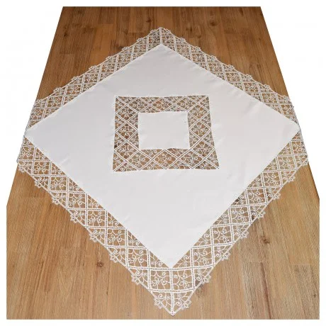 Ein weißes, quadratisches Tischtuch mit detaillierten Spitzenbordüren und ein passendes, mit Spitze eingefasstes Quadrat, das diagonal auf einem Holzboden liegt. Die Spitze zeigt feine geometrische und florale Motive.