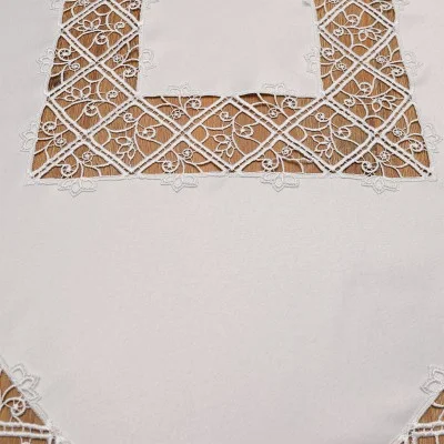 Nahaufnahme einer weißen Tischdecke mit Spitzenmuster an den Rändern. Die Spitze ist mit floralen und geometrischen Motiven bestickt, die transparente und detaillierte Muster bilden, die sich von dem unifarbenen Hintergrund abheben.