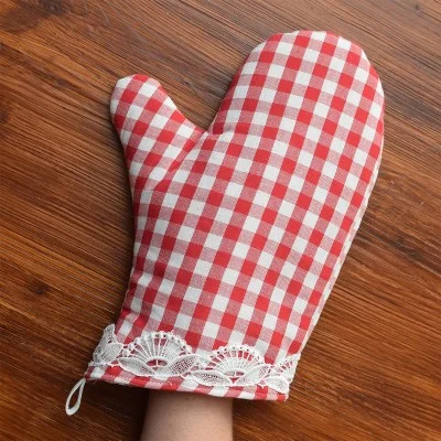 Eine Hand trägt einen rot-weiß karierten Topfhandschuh mit weißer Spitzenverzierung und ruht auf einer Holzfläche.