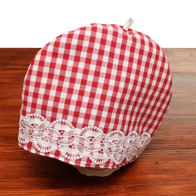 Nahaufnahme einer rot-weiß karierten Haube mit einem breiten Band aus weißer Spitze am unteren Rand, die auf einer hölzernen Oberfläche vor einem weißen Hintergrund ausgestellt ist.