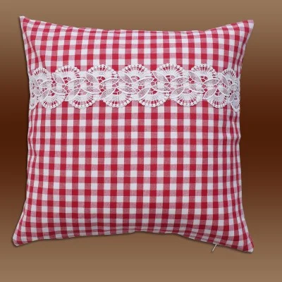 Ein quadratisches Kissen mit rot-weißem Karomuster und einem horizontalen Streifen weißer Spitze in der Mitte vor einem Hintergrund mit braunem Farbverlauf.