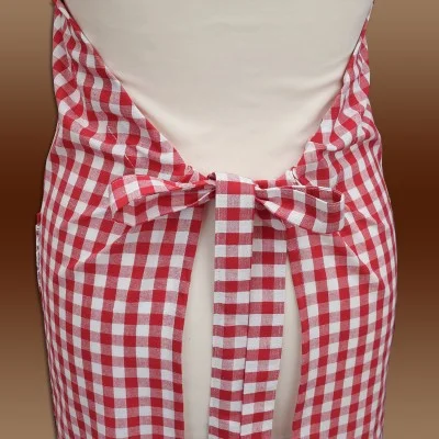 Nahaufnahme einer rot-weiß karierten Schürze, die mit einer hübschen Schleife am Rücken einer Person gebunden ist, die ein cremefarbenes Kleidungsstück trägt, mit einem weichen braunen Hintergrund.