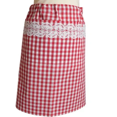 Eine knielange, rot-weiß karierte Schürze mit einem breiten horizontalen Band aus weißer Spitze auf der Vorderseite. Die Schürze wird an einer Schaufensterpuppe getragen und hat ein einfaches, klassisches Design, das an einen Vintage- oder Landhausküchenstil erinnert.
