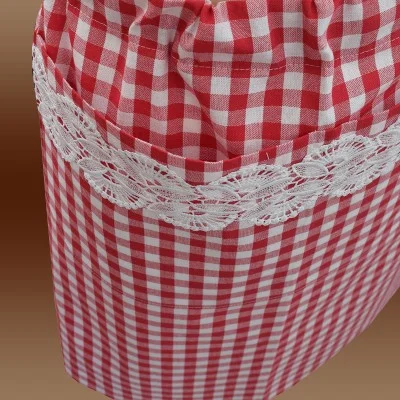 Eine Nahaufnahme eines rot-weiß karierten Stoffbeutels mit weißer Spitzenborte am oberen Rand vor einem braunen Hintergrund mit Farbverlauf. Das Täschchen ist oben gerafft, wodurch ein Rüscheneffekt entsteht.