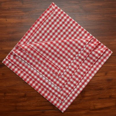 Eine rot-weiß karierte Stoffserviette ist diagonal auf einer dunklen Holzfläche ausgebreitet. Die Serviette hat einige sichtbare Knicke und Falten.