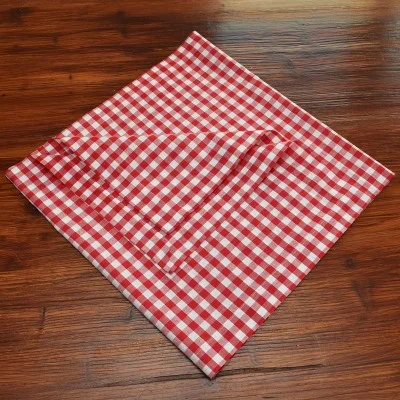 Eine rot-weiß karierte Serviette wird auf einer hölzernen Unterlage ordentlich zu einer Raute gefaltet.