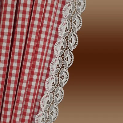 Rot-weiß karierter Stoff mit vertikalen Falten und einer dekorativen weißen Spitzenbordüre entlang der Kante vor einem Hintergrund mit braunem Farbverlauf.