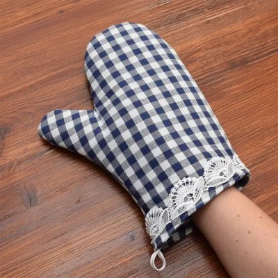 Eine Hand, die einen blau-weiß karierten Topfhandschuh mit weißer Spitzenborte am Handgelenk trägt, ruht auf einer Holzfläche.