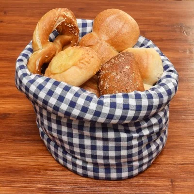 Ein blau-weiß-karierter Stoffkorb enthält verschiedene Brotsorten, darunter Brezeln, Brötchen und Brote. Der Korb steht auf einer polierten Holzfläche.