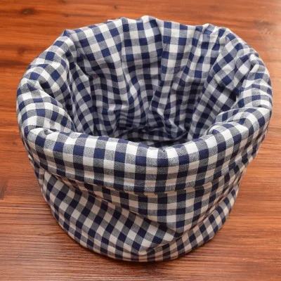 Ein blau-weiß karierter Stoffkorb liegt offen auf einer hölzernen Unterlage, wobei der Stoff einen weichen, runden Behälter bildet.