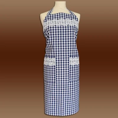 Eine Schaufensterpuppe zeigt eine blau-weiß karierte Schürze mit zwei Vordertaschen und weißem Spitzenbesatz auf der Brust und an den Taschen. Die Schürze hat einen Halsausschnitt und bedeckt den Körper bis knapp unterhalb der Knie. Der Hintergrund ist ein brauner Farbverlauf.