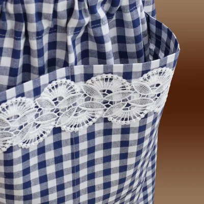 Nahaufnahme einer blau-weiß karierten Stoffschürze mit gerafftem Bund. Ein weißer Spitzenbesatz ziert den oberen Rand einer Seitentasche. Der Hintergrund besteht aus einem sanften Farbverlauf in Brauntönen.