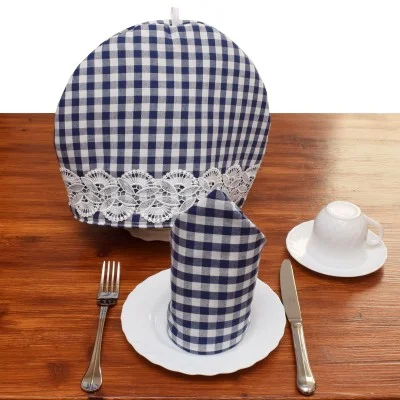 Ein zum Tee gedeckter Tisch mit Tasse und Untertasse, einem Teller mit gefalteter karierter Serviette, Besteck und einem blau-weiß karierten, mit Spitze verzierten Teewärmer, alles auf einer hölzernen Unterlage.