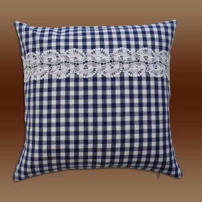 Ein quadratisches Kissen mit blau-weißem Karomuster und einem horizontalen Streifen dekorativer weißer Spitze auf der oberen Hälfte vor einem Hintergrund mit braunem Farbverlauf.