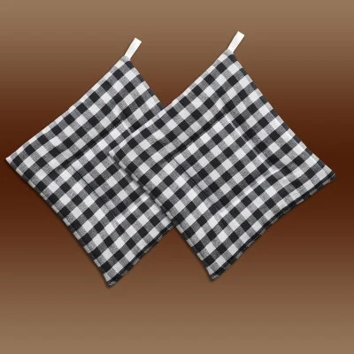 Zwei schwarz-weiß karierte Topflappen mit weißen Schleifen, diagonal angeordnet und überlappend auf einem braunen Hintergrund mit Farbverlauf.