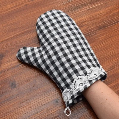 Eine Person, die einen schwarz-weiß karierten Topfhandschuh mit weißem Spitzenbesatz an der Hand trägt und auf einer Holzfläche ruht.