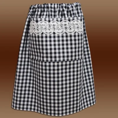 Eine schwarz-weiß karierte Schürze mit einer großen Tasche auf der Vorderseite. Die Tasche ist mit einem horizontalen Streifen aus weißer Spitze mit Blumenmuster verziert. Die Schürze hat einen gerafften, elastischen Bund. Der Hintergrund ist ein brauner Farbverlauf.