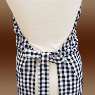 Nahaufnahme des Rückens eines Mannequins, das eine schwarz-weiß karierte Schürze trägt. Die Schürzenbänder werden in der Taille zu einer ordentlichen Schleife gebunden, wobei sich das Schachbrettmuster von dem einfarbigen cremefarbenen Hintergrund abhebt. Der Hintergrund ist ein brauner Farbverlauf.