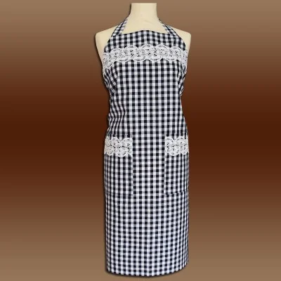 Eine Schaufensterpuppe zeigt eine schwarz-weiß karierte Schürze mit zwei Vordertaschen und weißem Spitzenbesatz im Brust- und Taschenbereich vor einem Hintergrund mit braunem Farbverlauf.