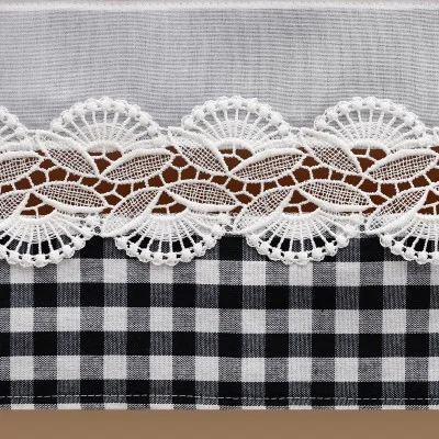 Nahaufnahme eines Stoffes mit einem schwarz-weiß karierten Muster im unteren Bereich, weißer Spitze mit komplizierten fächerförmigen Mustern in der Mitte und einfarbigem weißen Stoff im oberen Bereich. Die Spitze wirkt zart und ist gut sichtbar.