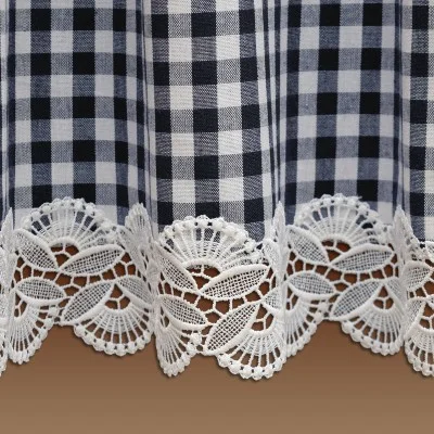 Nahaufnahme eines schwarz-weißen Gingham-Stoffes mit einem dekorativen Rand. Der Boden ist mit weißer Spitze mit Blumen- und Blattmustern verziert, die vor einem einfarbigen braunen Hintergrund stehen.