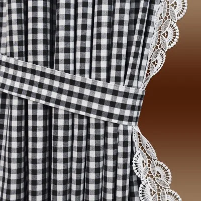 Nahaufnahme eines schwarz-weiß karierten Vorhangs mit passender Raffhalterung und weißer Spitzenborte am Rand. Der Hintergrund ist ein brauner Farbverlauf.