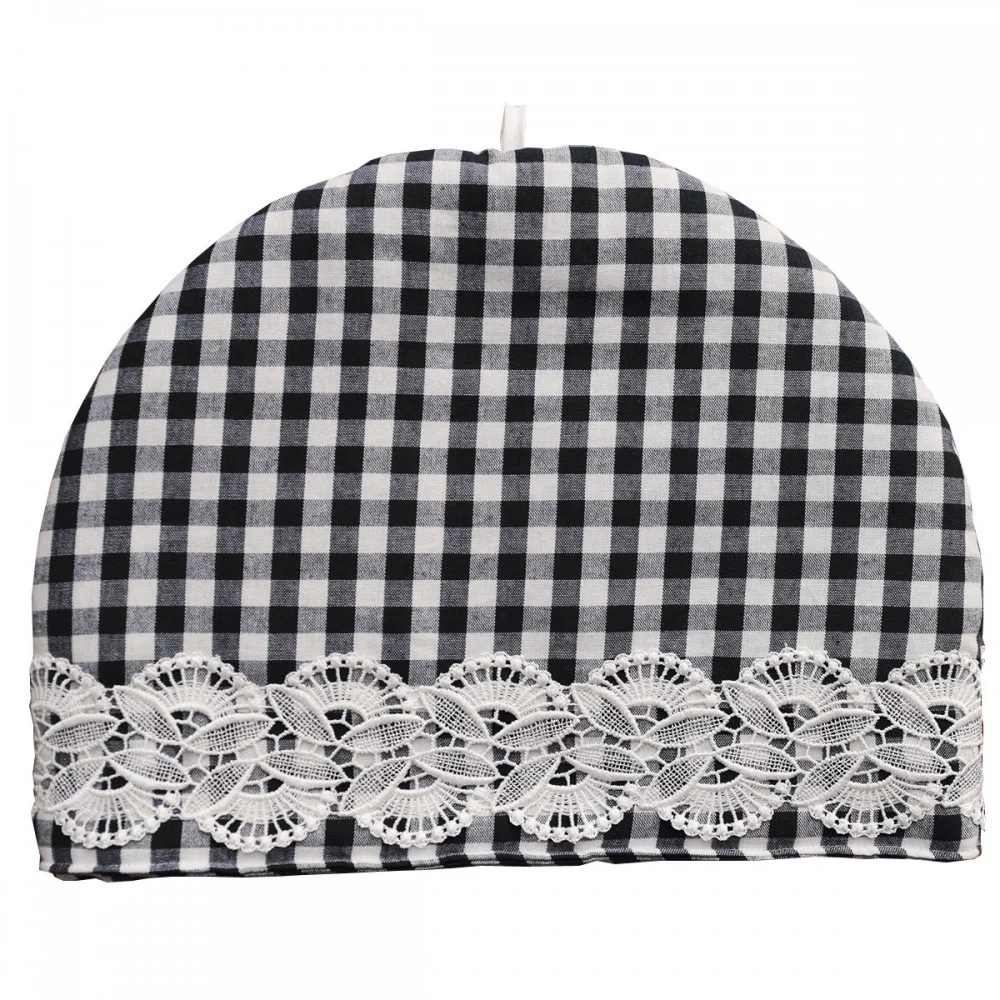 Ein schwarz-weiß karierter Teewärmer mit abgerundeter Oberseite. Der untere Rand ist mit einem breiten Streifen weißer Spitze mit floralem Muster verziert. In der oberen Mitte ist eine kleine weiße Schleife angebracht. Der Hintergrund ist einfarbig und weiß.