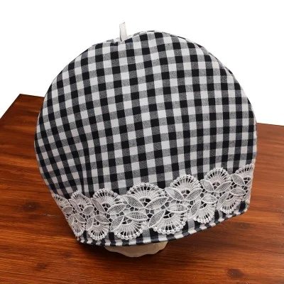 Eine schwarz-weiß karierte Stoffkuppel mit einem breiten Band aus filigraner weißer Spitze am unteren Rand steht auf einer Holzfläche. Der Hintergrund ist weiß und hebt die detaillierte Spitze und das kontrastierende Karomuster hervor.