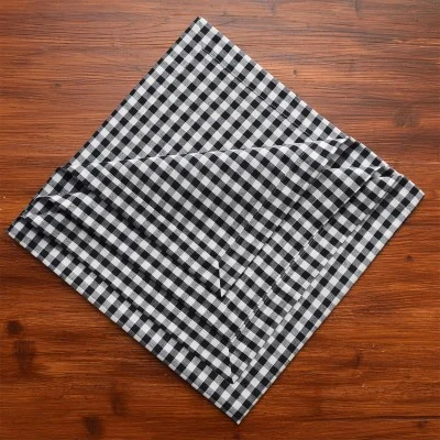 Eine schwarz-weiß karierte Stoffserviette wird diagonal auf einem Holztisch mit sichtbarer Maserung ausgebreitet.